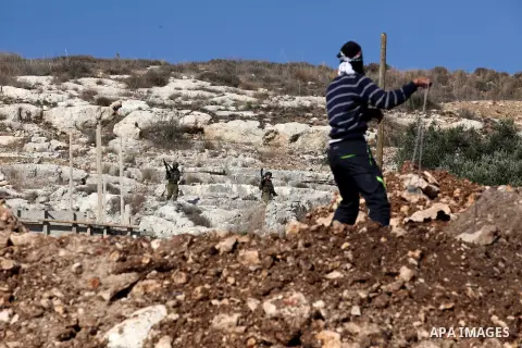 A Palestinian protester uses a slingshot to hurl stones towards Israeli security forces during clashes following a demonstration against the expropriation of Palestinian land by Israel in the village of Kfar Qaddum, near...