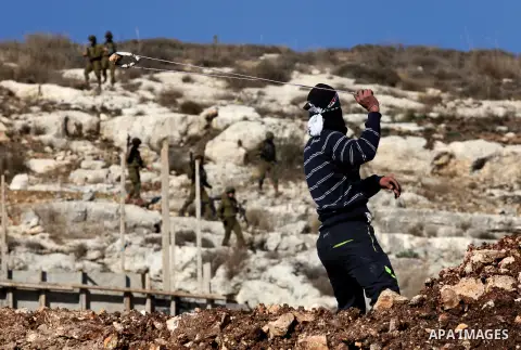 A Palestinian protester uses a slingshot to hurl stones towards Israeli security forces during clashes following a demonstration against the expropriation of Palestinian land by Israel in the village of Kfar Qaddum, near...