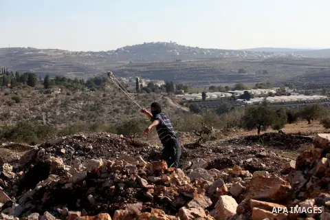 A Palestinian protester uses a slingshot to hurl stones towards Israeli security forces during clashes following a demonstration against the expropriation of Palestinian land by Israel in the village of Kfar Qaddum, near...