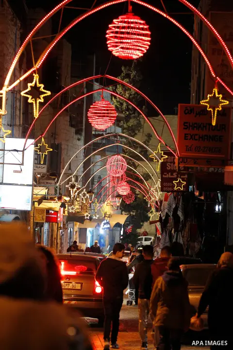 Palestinian Christians walk under lights decorating at the Manger Square near the Church of the Nativity, in the biblical West Bank town of Bethlehem on December 11, 2016. Photo by Wisam Hashlamoun