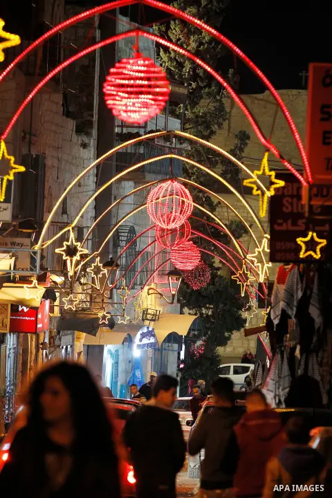 Palestinian Christians walk under lights decorating at the Manger Square near the Church of the Nativity, in the biblical West Bank town of Bethlehem on December 11, 2016. Photo by Wisam Hashlamoun