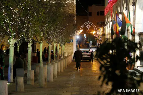 Palestinian Christians walk under lights decorating at the Manger Square near the Church of the Nativity, in the biblical West Bank town of Bethlehem on December 11, 2016. Photo by Wisam Hashlamoun