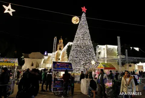 Palestinian Christians walk in front of a Christmas tree at the Manger Square near the Church of the Nativity, in the biblical West Bank town of Bethlehem on December 11, 2016. Photo by Wisam Hashlamoun