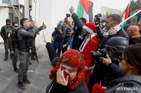 Palestinian protestors, some dressed up as Santa Claus, demonstrate next to a gate at a section of Israel's separation wall in the biblical town of Bethlehem, in the occupied West Bank, on December 23, 2016. Photo by Wis...
