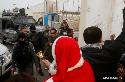 Palestinian protestors, some dressed up as Santa Claus, demonstrate next to a gate at a section of Israel's separation wall in the biblical town of Bethlehem, in the occupied West Bank, on December 23, 2016. Photo by Wis...
