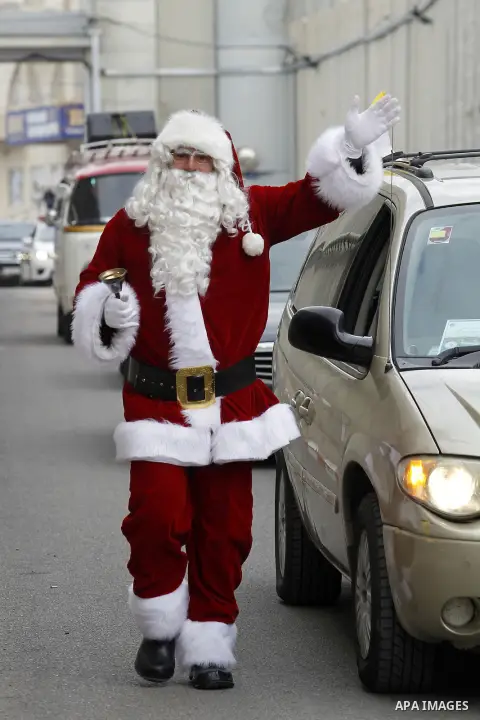 A Palestinian dressed as Santa Claus gestures as the Latin Patriarch of Jerusalem Pierbattista Pizzaballa arrives through an Israeli checkpoint to attend Christmas celebrations, in the city of Bethlehem in the Israeli-oc...