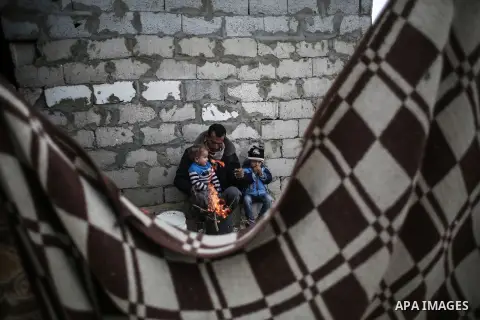 A Palestinian man and his children warm themselves around the fire during rainy, cold weather outside their house in a slum on the outskirts of Khan Younis refugee camp, southern Gaza Strip, on December 28, 2016. Photo b...
