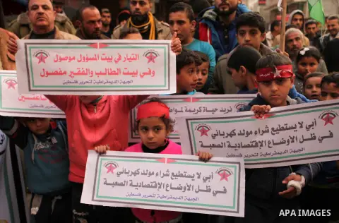 Palestinian children hold placards and light candles during a protest against a power cut in Bureij refugee camp, central Gaza Strip, on January 3, 2017. Photo by Ashraf Amra
