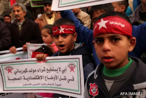Palestinian children hold placards and light candles during a protest against a power cut in Bureij refugee camp, central Gaza Strip, on January 3, 2017. Photo by Ashraf Amra