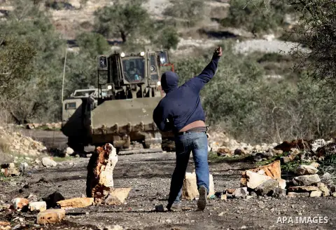 A Palestinian protester hurls stones towards a digger operated by Israeli security forces during clashes following a demonstration against the expropriation of Palestinian land by Israel in the village of Kfar Qaddum, ne...