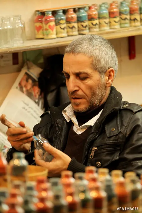 A Palestinian man paints on glass pots using colored sand, at his work shop in the Old City of the West Bank town of Hebron, on January 25, 2017. Photo by Wisam Hashlamoun