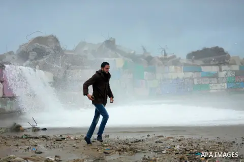 A Palestinian man runs as a huge wave crash over a sea wall at the Gaza seaport during a rainy and heavy wind weather prevails on the Mediterranean Sea, in Gaza City on January 28, 2017. Photo by Mohammed Asad