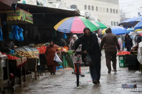 Palestinians walk through a wet street during a rainy day at a market at the Al-Shati refugee camp in Gaza City on February 14, 2017. Photo by Mohammed Asad