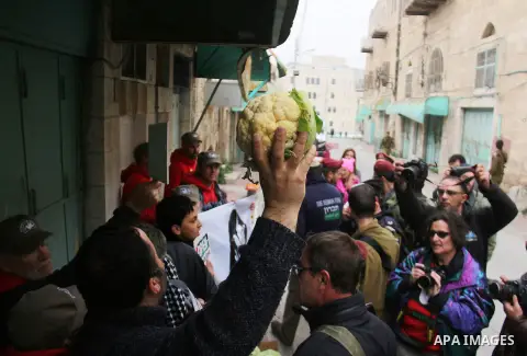 A Palestinian protester sells vegetables in front of Israeli Settlers during a demonstration against the closure of Shuhada street, on the 23rd anniversary of the closure, on February 22, 2017 in the West Bank city of He...