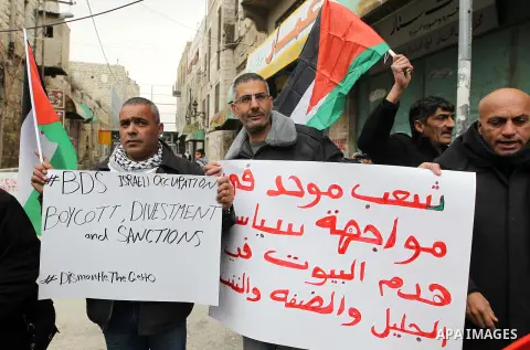 Palestinian protesters hold placards during a demonstration against the closure of Shuhada street, on the 23rd anniversary of the closure, on February 22, 2017 in the West Bank city of Hebron. On February 25, 1994 Israel...