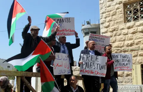 Palestinian demonstrators hold national flags and placards during a protest against Jewish settlements in the West Bank city of Hebron March 26, 2017. Photo by Wisam Hashlamoun
