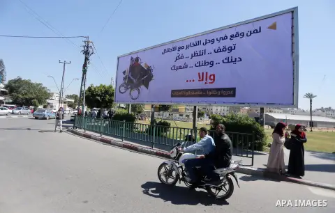 Palestinians walk past a banner announcing the launch of a campaign against collaborating with Israel, in Gaza city, on April 04, 2017, as the ruling Ministry of Interior in the Gaza Strip launches a week-long campaign t...