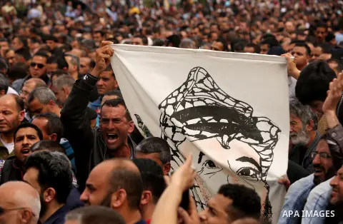 A Palestinian Authority employee holds a painted poster depicting late Palestinian leader Yasser Arafat during a demonstration against the decision to reduce their salaries in Gaza City on April 8, 2017. Photo by Ashraf...