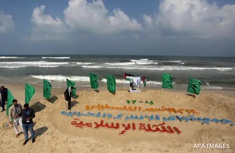 Palestinians stand next to an art installation by a Palestinian artist Mohammed Totah which he outlines in sand to mark the Palestinian Prisoner day, on Gaza City's Mediterranean shore on April 15, 2017. Photo by Ashraf...