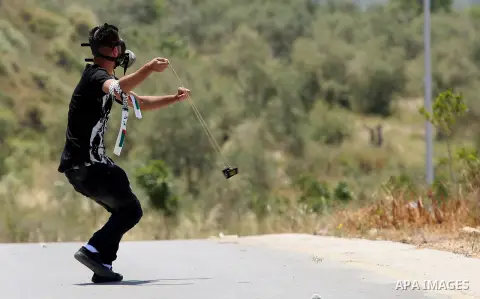 A Palestinian protester uses a slingshot to hurl stones towards Israeli security forces during clashes at a protest in support of Palestinian prisoners on hunger strike in Israeli jails, in the West Bank village of al-Na...