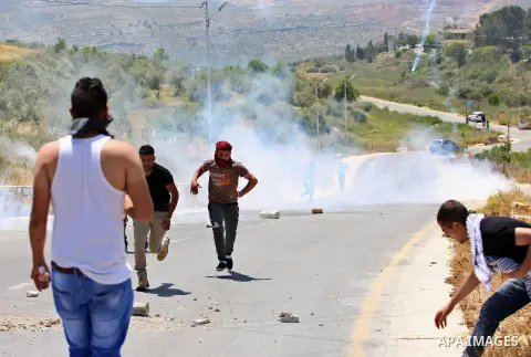 Palestinian protesters run for a cover from a tear gas canister fired by Israeli security forces during clashes at a protest in support of Palestinian prisoners on hunger strike in Israeli jails, in the West Bank village...