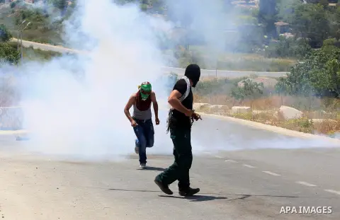 Palestinian protesters run for a cover from a tear gas canister fired by Israeli security forces during clashes at a protest in support of Palestinian prisoners on hunger strike in Israeli jails, in the West Bank village...