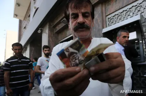 Palestinians, employed by the Palestinian Authority wait to receive their salaries from an ATM, outside a Bank in Gaza City on May 10, 2017. The salaries of Palestinian employees in Gaza strip have been reduced by about...