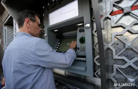 Palestinians, employed by the Palestinian Authority wait to receive their salaries from an ATM, outside a Bank in Gaza City on May 10, 2017. The salaries of Palestinian employees in Gaza strip have been reduced by about...