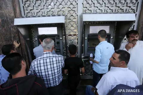 Palestinians, employed by the Palestinian Authority wait to receive their salaries from an ATM, outside a Bank in Gaza City on May 10, 2017. The salaries of Palestinian employees in Gaza strip have been reduced by about...