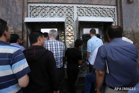 Palestinians, employed by the Palestinian Authority wait to receive their salaries from an ATM, outside a Bank in Gaza City on May 10, 2017. The salaries of Palestinian employees in Gaza strip have been reduced by about...