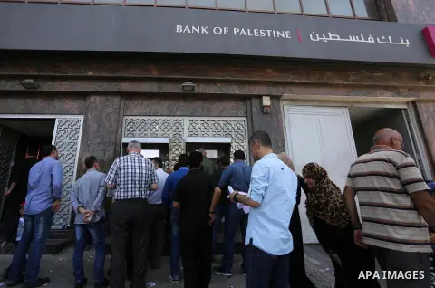 Palestinians, employed by the Palestinian Authority wait to receive their salaries from an ATM, outside a Bank in Gaza City on May 10, 2017. The salaries of Palestinian employees in Gaza strip have been reduced by about...