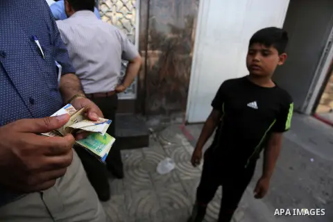 Palestinians, employed by the Palestinian Authority wait to receive their salaries from an ATM, outside a Bank in Gaza City on May 10, 2017. The salaries of Palestinian employees in Gaza strip have been reduced by about...