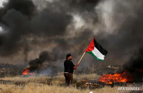 A Palestinian protester waves the national flag during clashes with Israeli security forces following a protest against the blockade on Gaza Strip, near the border fence east of Gaza City on May 22, 2017. Photo by Ashraf...