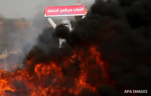 A Palestinian protester holds placards near burning tires during clashes with Israeli security forces following a protest against the blockade on Gaza Strip, near the border fence east of Gaza City on May 22, 2017. Photo...