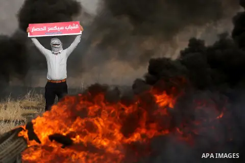 A Palestinian protester holds placards near burning tires during clashes with Israeli security forces following a protest against the blockade on Gaza Strip, near the border fence east of Gaza City on May 22, 2017. Photo...