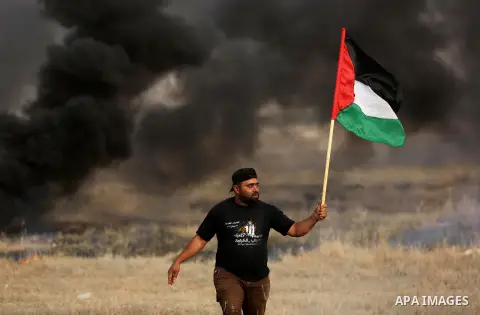 A Palestinian protester waves the national flag during clashes with Israeli security forces following a protest against the blockade on Gaza Strip, near the border fence east of Gaza City on May 22, 2017. Photo by Ashraf...