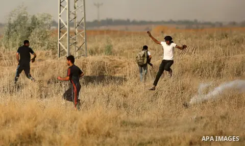 Palestinian protesters run for cover from tear gas canister fired by Israeli security forces during clashes following a protest against the blockade on Gaza Strip, near the border fence east of Gaza City on May 22, 2017....
