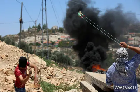 A Palestinian protester uses a slingshot to hurl stones towards Israeli security forces during clashes following a demonstration against the expropriation of Palestinian land by Israel in the village of Kfar Qaddum, near...