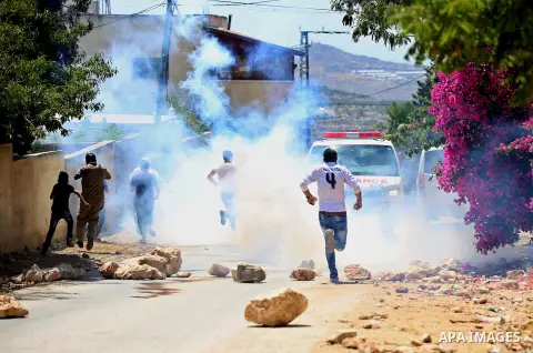 Palestinian protesters run for a cover from a tear gas canister fired by Israeli security forces during clashes following a demonstration against the expropriation of Palestinian land by Israel in the village of Kfar Qad...