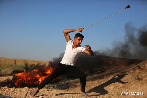 A Palestinian protester uses a slingshot to hurl stones towards Israeli security forces during clashes following a demonstration against the blockade on the Gaza Strip, near the border fence east of Jabalia refugee camp...