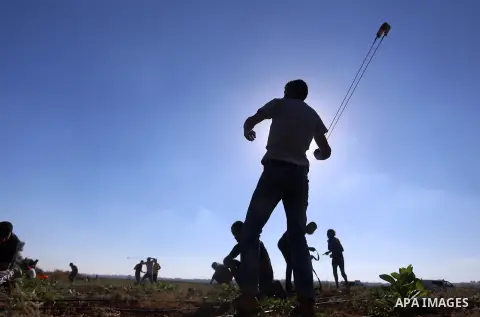 A Palestinian protester uses a slingshot to hurl stones towards Israeli security forces during clashes following a demonstration against the blockade on the Gaza Strip, near the border fence east of Jabalia refugee camp...