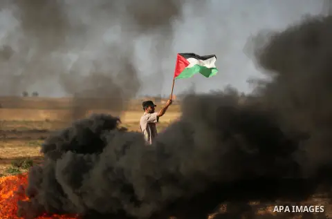 A protester holds a Palestinian flag during clashes with Israeli troops at a protest against reducing power supply to Gaza, near the border with Israel in Khan Younis in the southern Gaza Strip June 20, 2017. Photo by As...