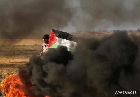 A protester holds a Palestinian flag during clashes with Israeli troops at a protest against reducing power supply to Gaza, near the border with Israel in Khan Younis in the southern Gaza Strip June 20, 2017. Photo by As...