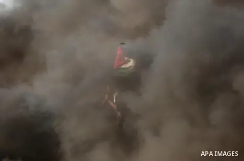 A protester holds a Palestinian flag during clashes with Israeli troops at a protest against reducing power supply to Gaza, near the border with Israel in Khan Younis in the southern Gaza Strip June 20, 2017. Photo by As...