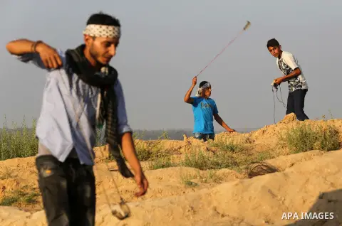 Palestinian protesters use slingshots to hurl stones towards Israeli security forces during clashes near the border between Israel and Central Gaza Strip August 11, 2017. Photo by Ashraf Amra