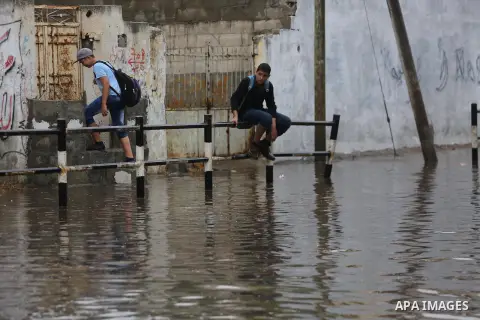 Palestinian students walk in a street flooded by rain water, in Gaza city on October 9, 2017. Photo by Mohammed Asad