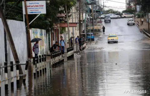 Palestinian students walk in a street flooded by rain water, in Gaza city on October 9, 2017. Photo by Mohammed Asad