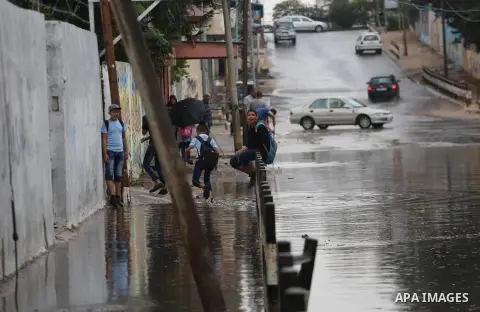 Palestinian students walk in a street flooded by rain water, in Gaza city on October 9, 2017. Photo by Mohammed Asad