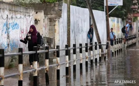 Palestinian students walk in a street flooded by rain water, in Gaza city on October 9, 2017. Photo by Mohammed Asad