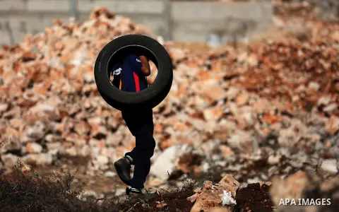 A Palestinian protester carries a car tire during clashes with Israeli security forces following a weekly demonstration against the expropriation of Palestinian land by Israel in the village of Kfar Qaddum, near Nablus i...